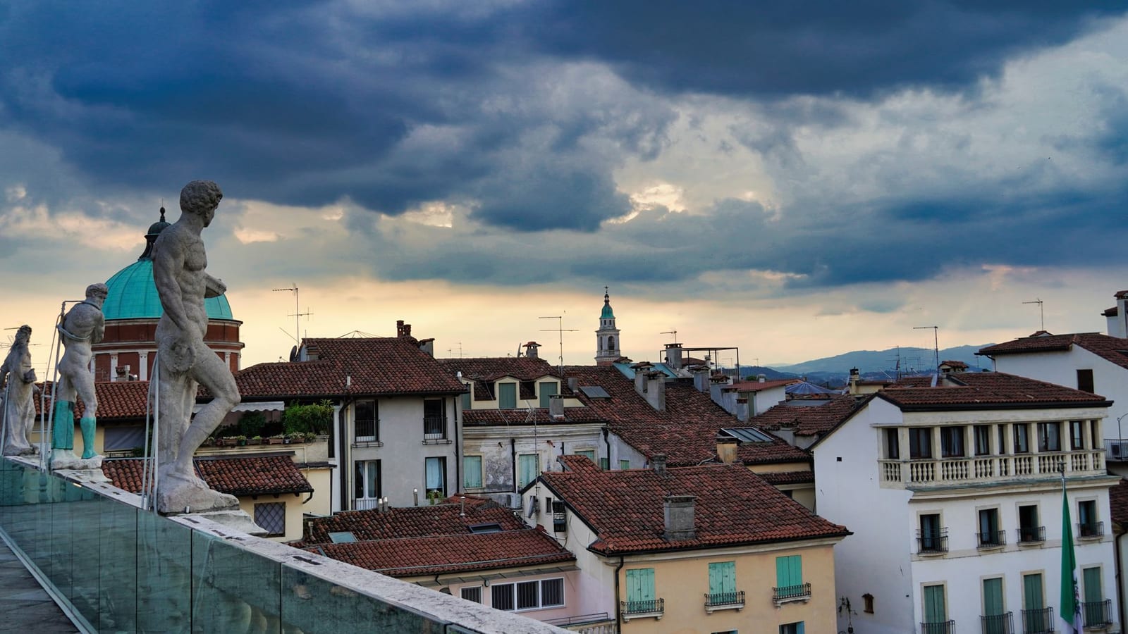 I tetti del centro di Vicenza con le statue e il campanile, sotto un cielo drammatico